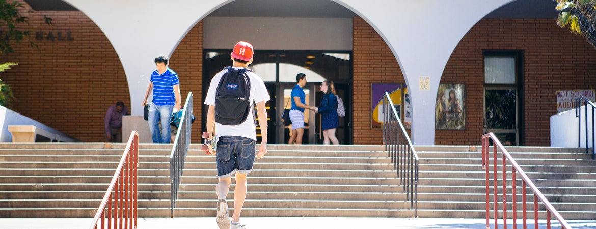 A UCR student holds a skateboard as they walk up the steps to Olmsted Hall.