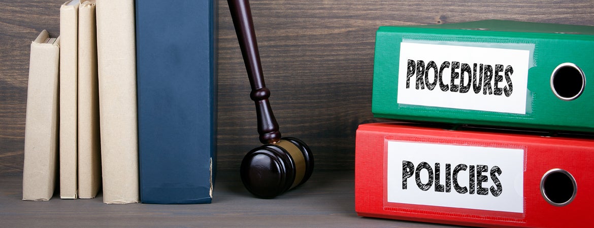 Academic Integrity Policies and Procedures Binders containing policies and procedures sit on a shelf with a gavel and books.